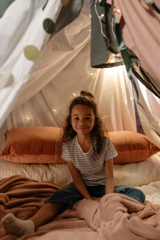 a little girl that is sitting on a bed, glamping, barrel fires and tents, gen z, fairy lights