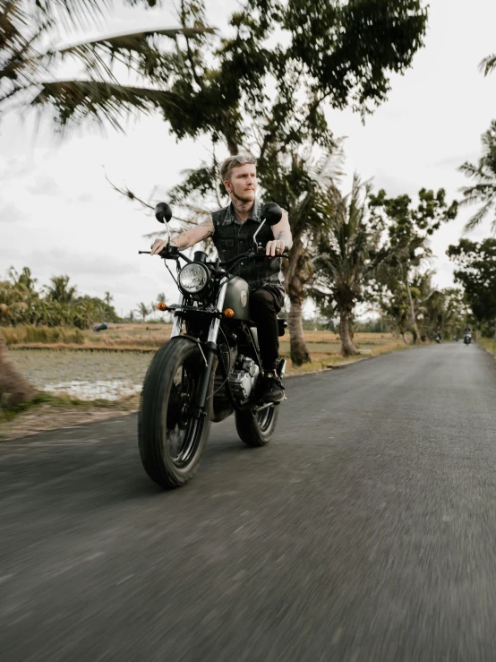 a man riding on the back of a motorcycle down a road, an album cover, by Kristian Zahrtmann, pexels contest winner, bali, portrait shot 8 k, black, action scene screenshot