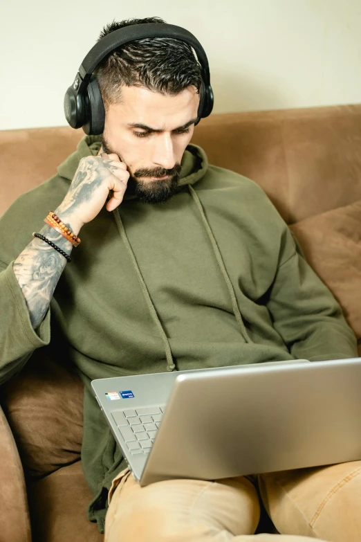 a man sitting on a couch with a laptop and headphones, trending on pexels, tattooed, wearing a green sweater, militaristic, avatar image