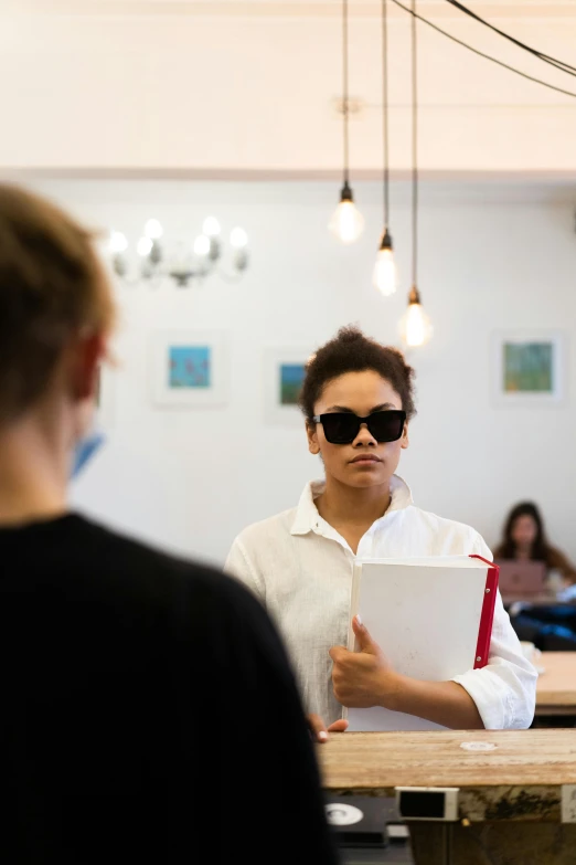 a woman that is standing in front of a counter, trending on unsplash, art & language, standing in class, wearing shades, actors, on a white table