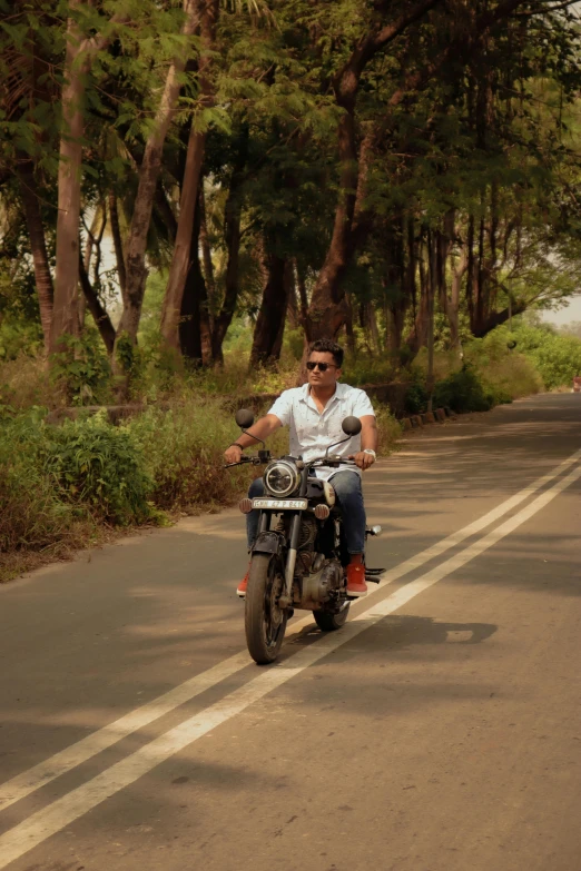 a man riding on the back of a motorcycle down a road, indian forest, smirking, college, on the coast