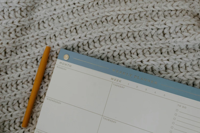 a notepad sitting on top of a blanket next to a pencil, inspired by Agnes Martin, trending on pexels, light grey blue and golden, made of wool, detail shot, female calendar