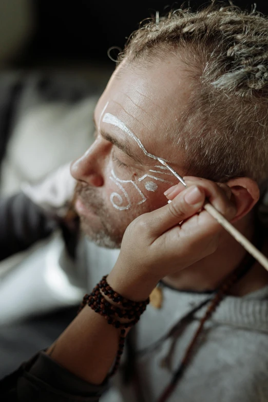 a man with some white paint on his face, an airbrush painting, trending on pexels, renaissance, scandinavian / norse influenced, putting makeup on, aboriginal engraving, eye art