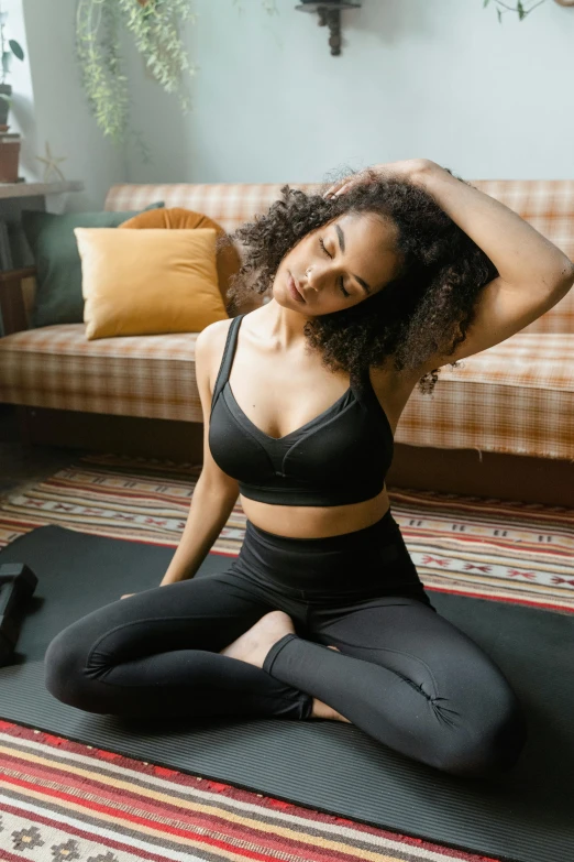 a young african woman sits in a black sports top while doing yoga