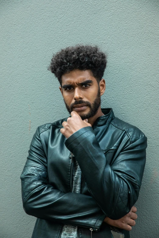 a man in a leather jacket leaning against a wall, by Cosmo Alexander, trending on pexels, renaissance, imaan hammam, serious and stern expression, solid background, peruvian looking