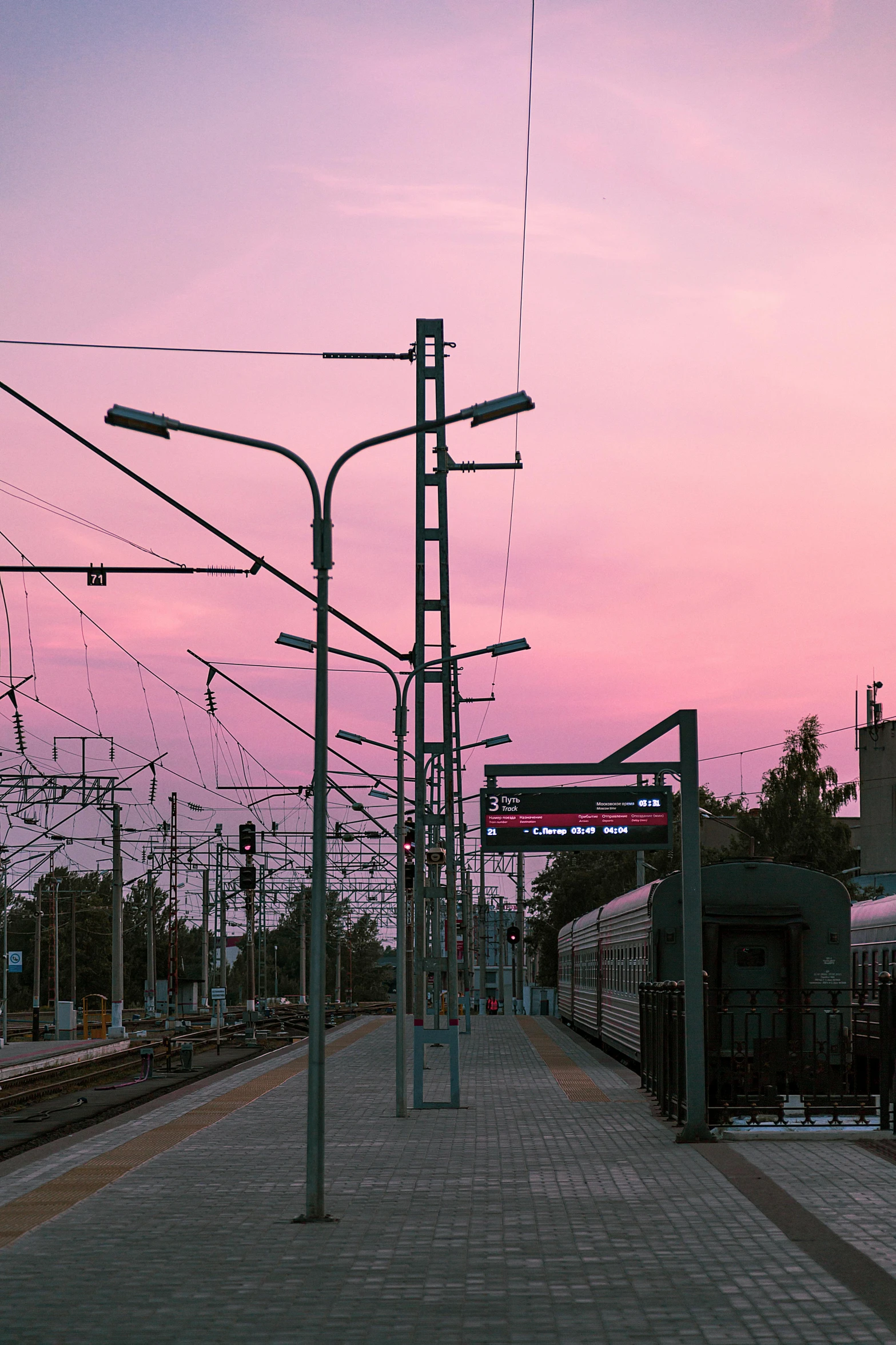 a train traveling down train tracks next to a train station, a picture, by Sven Erixson, unsplash, pink sky, telephone wires, at purple sunset, trip to legnica