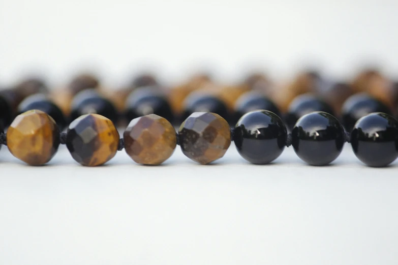 a row of tiger eye beads on a white surface, unsplash, black and brown, faceted, close up angle, gemstone necklace