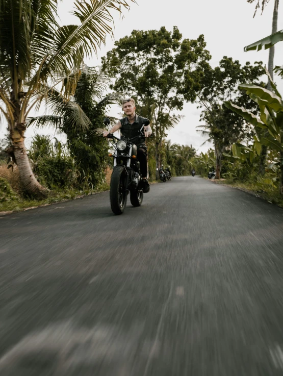 a man riding on the back of a motorcycle down a road, inspired by Alex Petruk APe, sumatraism, black sand, matt finish, promo image, trees in the background