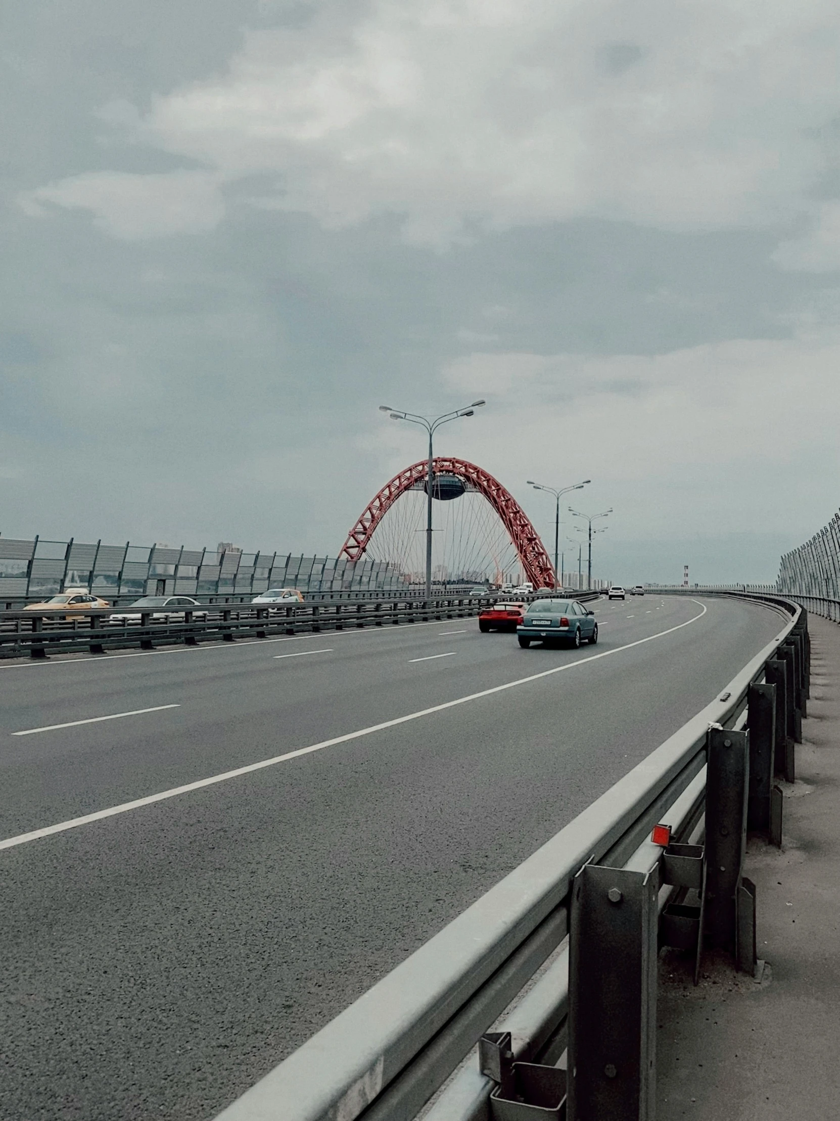 cars driving on a road near a bridge under a cloudy sky