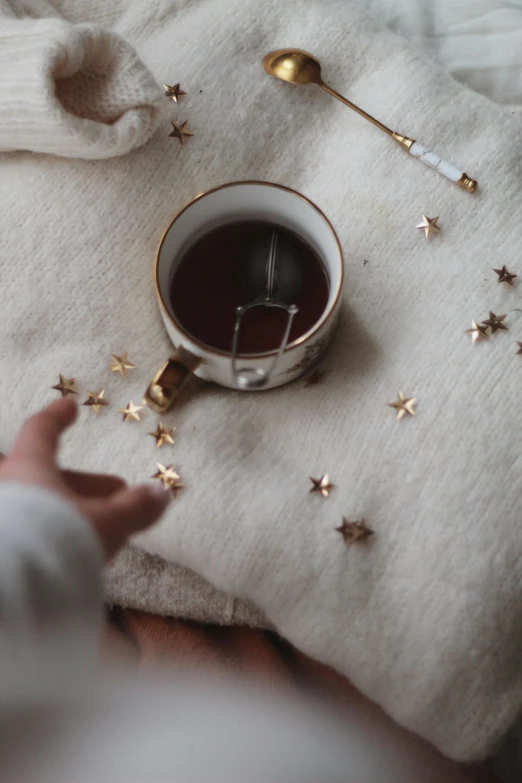 a close up of a person holding a cup of coffee, a cross stitch, by Julia Pishtar, trending on pexels, aestheticism, glittering stars scattered about, made of wool, is ((drinking a cup of tea)), chocolate