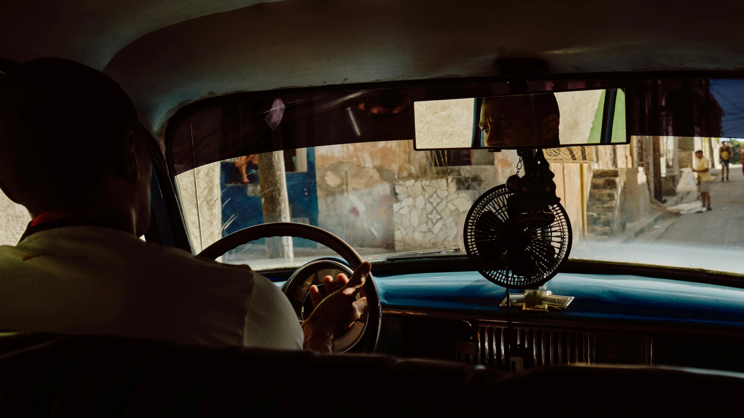 a man sitting in the driver's seat of a car, an album cover, by Elsa Bleda, pexels contest winner, cuban women in havana, interior of a small, fan favorite, dimly lit room