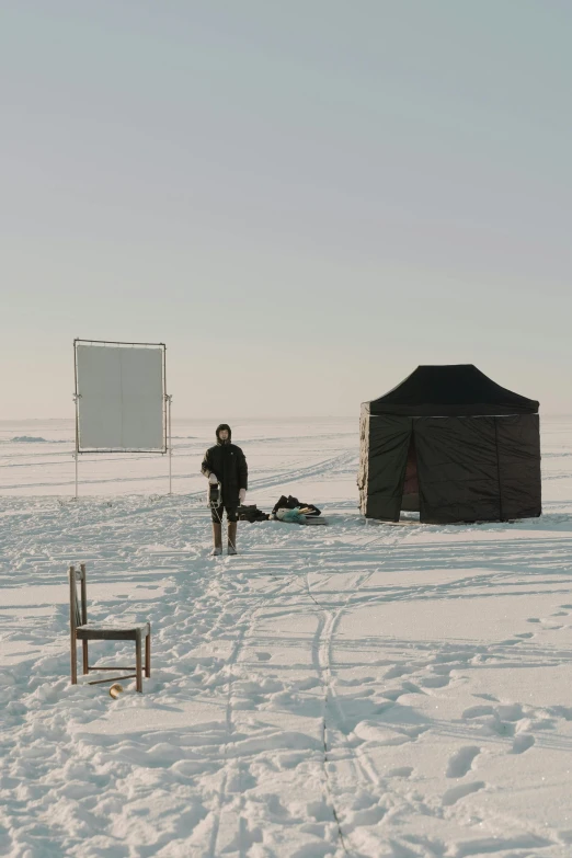 a man standing on top of a snow covered field, an album cover, inspired by Einar Hakonarson, temporary art, stands at a his easel, large screen, set photograph in costume, camp