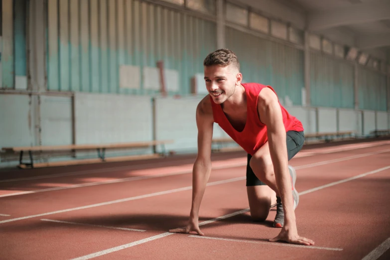 the man is stretching on his knees on a red running track