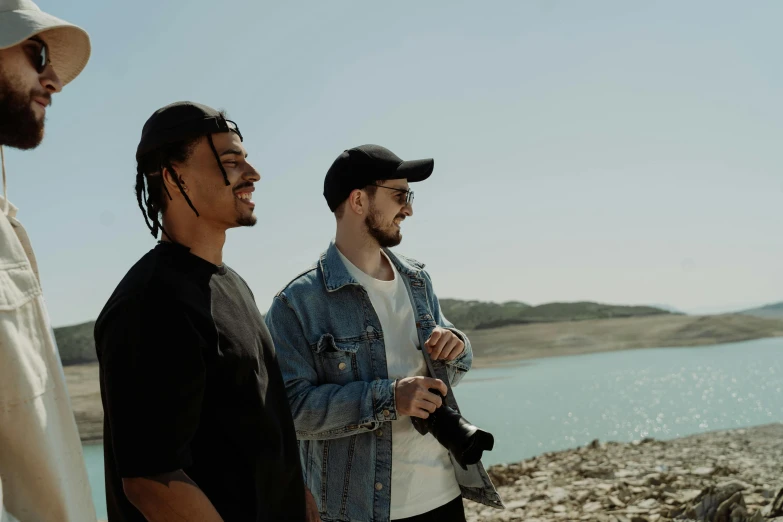 a group of men standing next to each other near a body of water, a picture, pexels contest winner, bowater charlie and brom gerald, performing a music video, a photo of a lake on a sunny day, portrait of two people