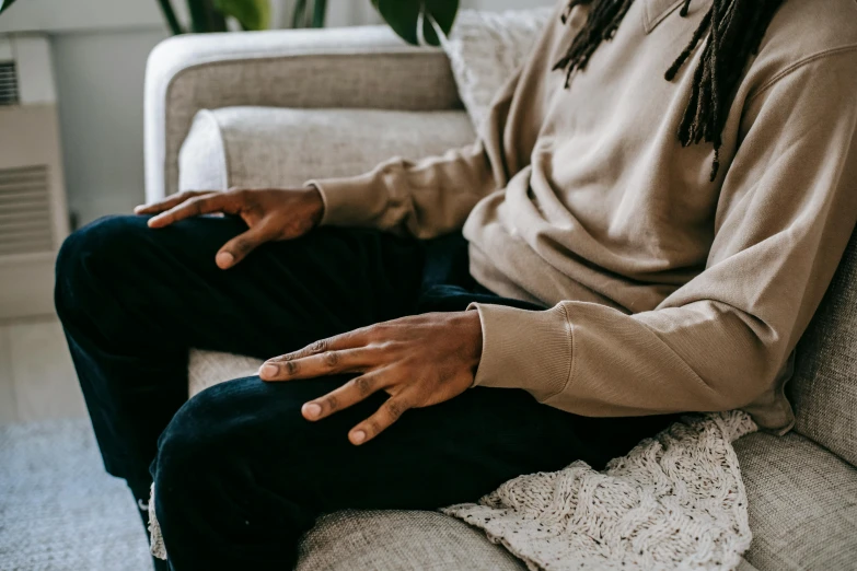 a man with dreadlocks sitting on a couch, by Nina Hamnett, trending on pexels, beige hoodie, hand on hip, sleek hands, federation clothing