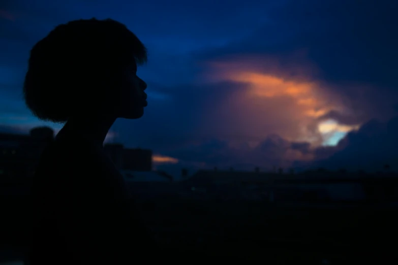 a silhouette of a person standing in front of a dark sky, a portrait, by Max Dauthendey, pexels contest winner, realism, black teenage boy, orange and blue sky, with thunderstorms, face shot