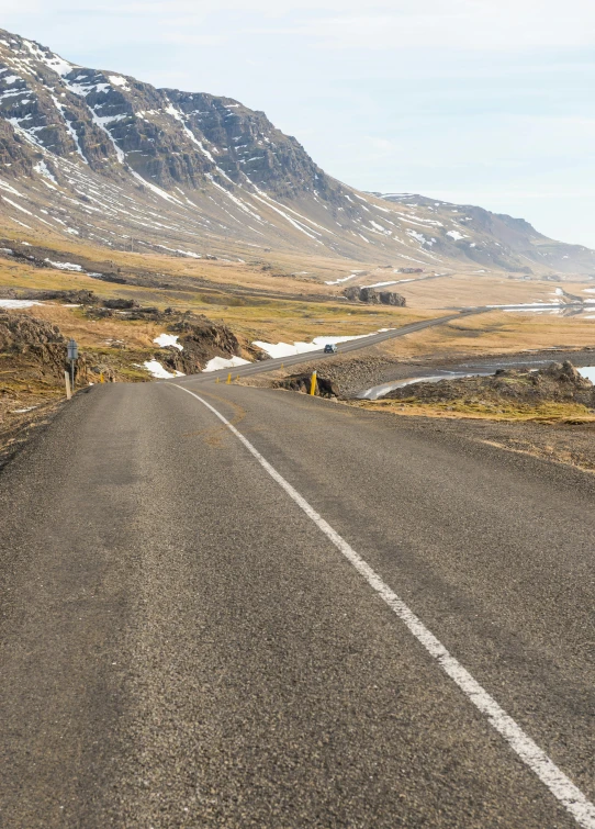 an empty road near mountains with snow on top