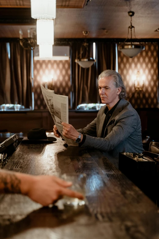 a man sitting at a bar reading a newspaper, a portrait, by Jakob Emanuel Handmann, unsplash, private press, pierce brosnan, david spade, gray haired, holding a record