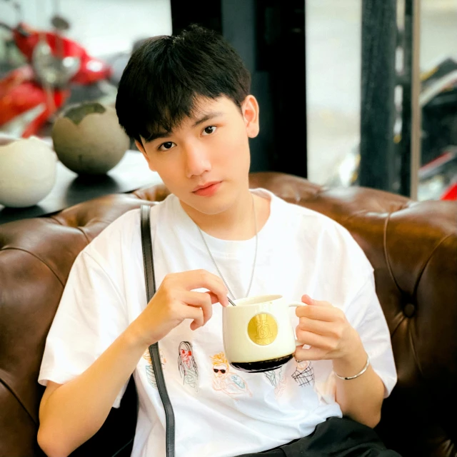 a man sitting on a couch holding a cup of coffee, inspired by Bian Shoumin, instagram, shin hanga, he is about 20 years old | short, profile image, avatar image, “ golden chalice
