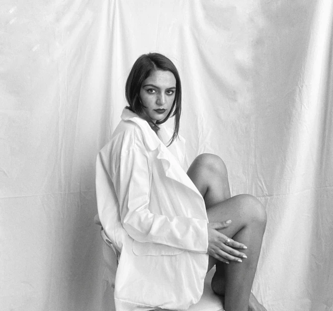 a black and white photo of a woman sitting on a toilet, by Emma Andijewska, realism, white silky outfit, white jacket, white backdrop, portrait sophie mudd