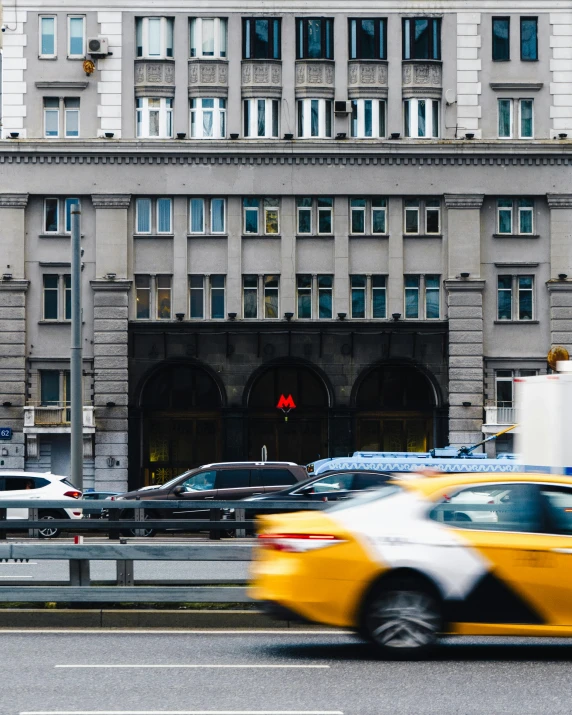 a yellow taxi driving down a street next to a tall building, a photo, by Emma Andijewska, pexels contest winner, art nouveau, moscow metro, non-binary, massive arch, gif