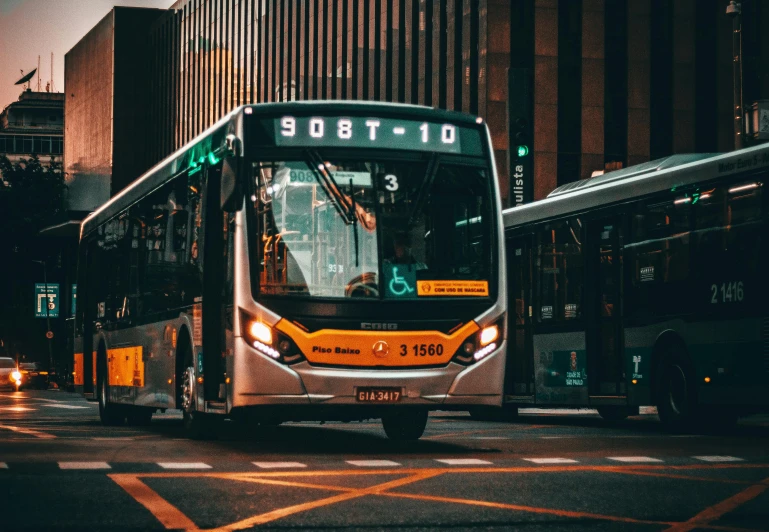 a bus driving down a street next to tall buildings, pexels contest winner, with orange street lights, avatar image, buses, sitting down