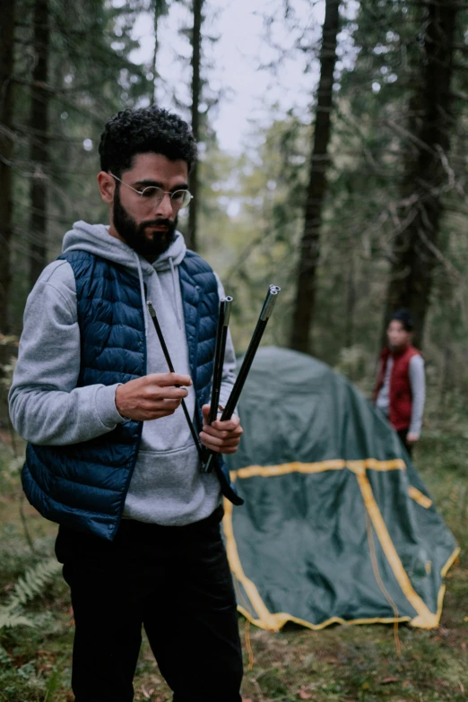 a man standing next to a tent in the woods, holding a small vape, student, amr elshamy, holding sabre