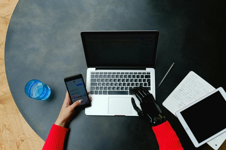 a person sitting at a table with a laptop and cell phone, trending on pexels, prosthetic arm, black and red only, avatar image, flatlay