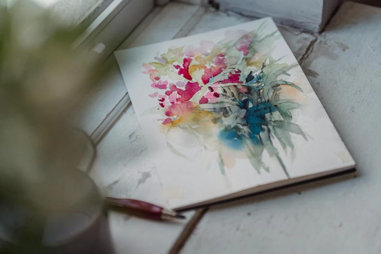 a book sitting on a window sill next to a potted plant, a watercolor painting, inspired by François Boquet, unsplash, process art, colourful flowers bouquet, on a white table, pencil and paper, moody light