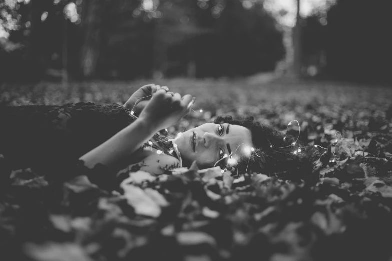 a black and white photo of a woman laying in the leaves, by irakli nadar, tumblr, fairy lights, unsplash photo contest winner, miniature photography, cute