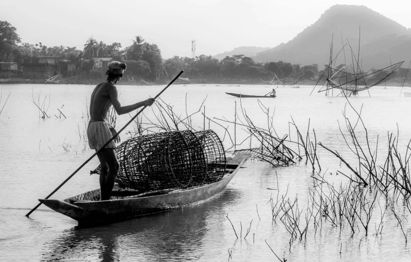 a black and white photo of a man in a boat, by Sunil Das, pexels contest winner, environmental art, nest is made of sticks, vibrant scene, early evening, fish flocks