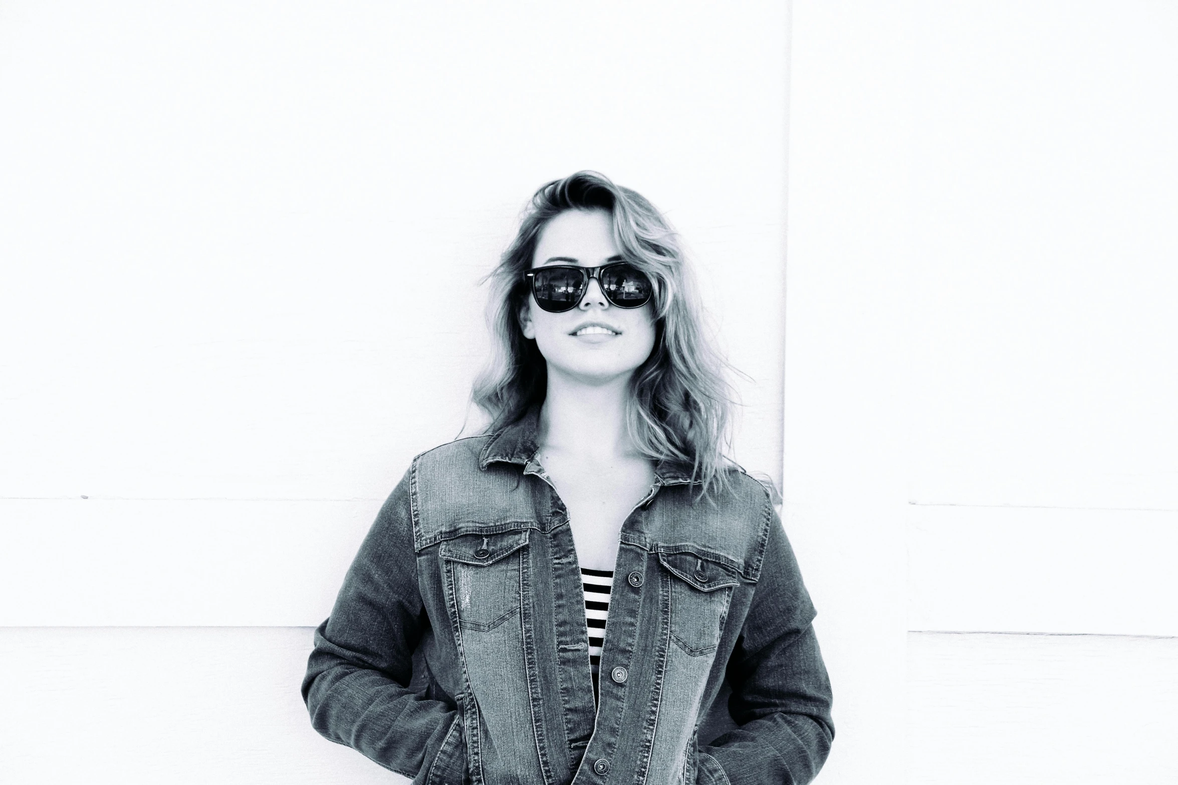 a woman standing in front of a white wall, a black and white photo, with sunglass, wearing a jeans jackets, instagram photo, trending photo