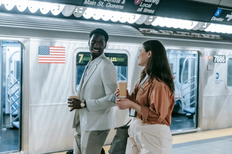 a couple of people standing next to a train, in new york, brown and white color scheme, people shopping, supportive