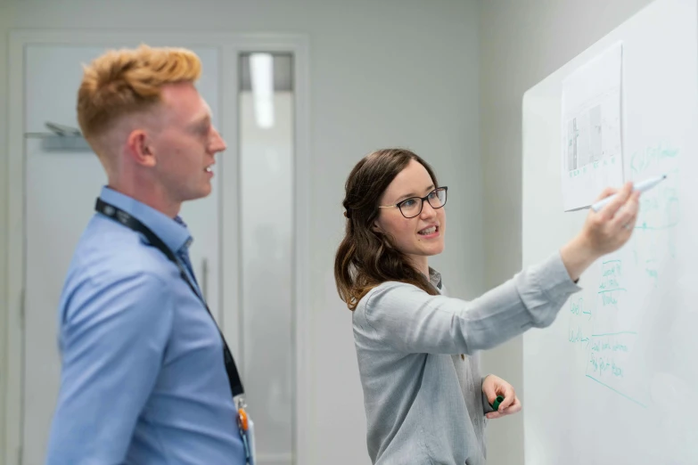 a man and a woman standing in front of a whiteboard, by Gavin Nolan, in an call centre office, kyle mclaughlin, profile image, opening shot