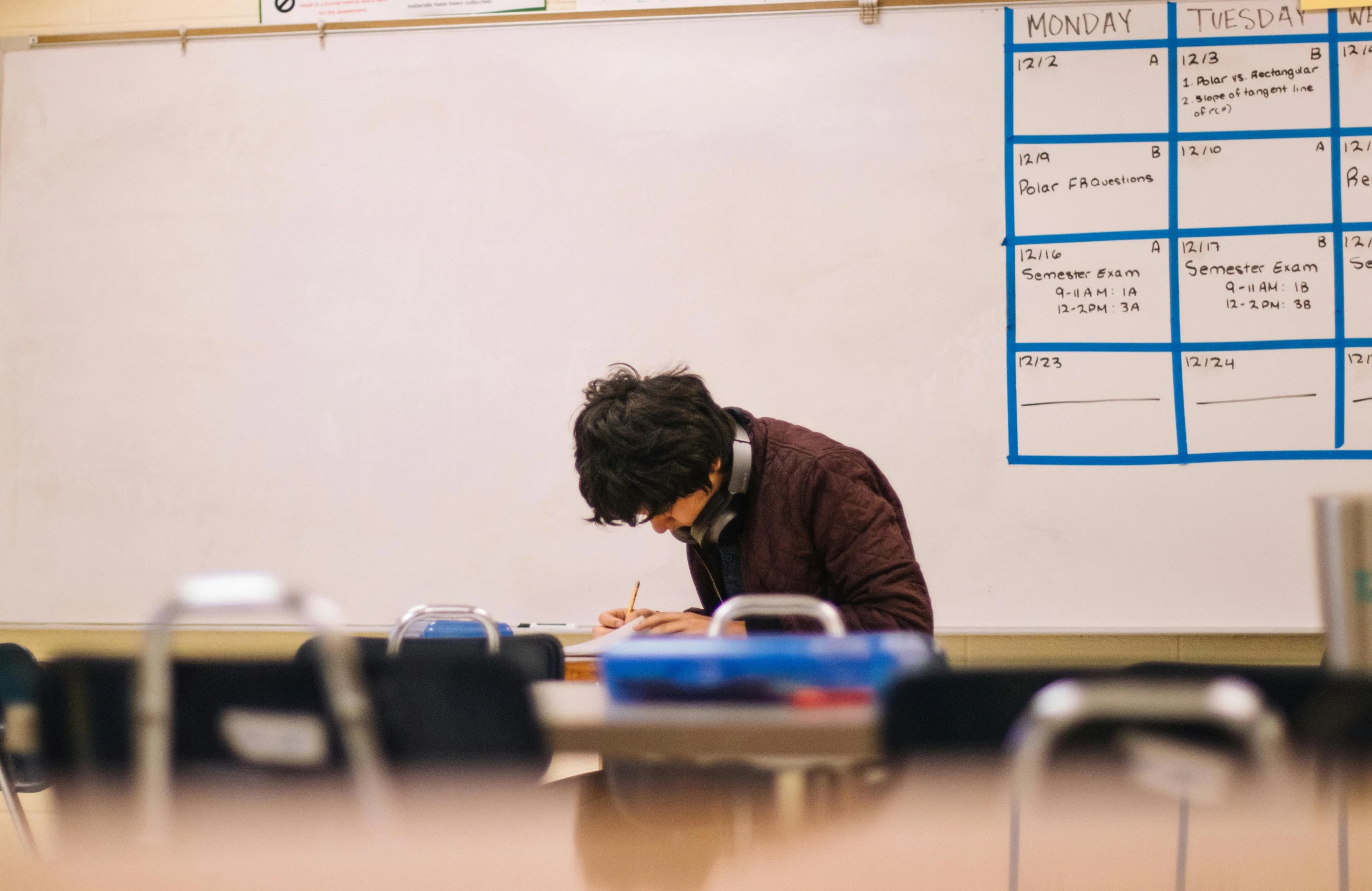 a man sitting at a desk writing on a piece of paper, by Jang Seung-eop, pexels contest winner, ashcan school, whiteboards, sitting alone, ethan klein, takeyuki kanda