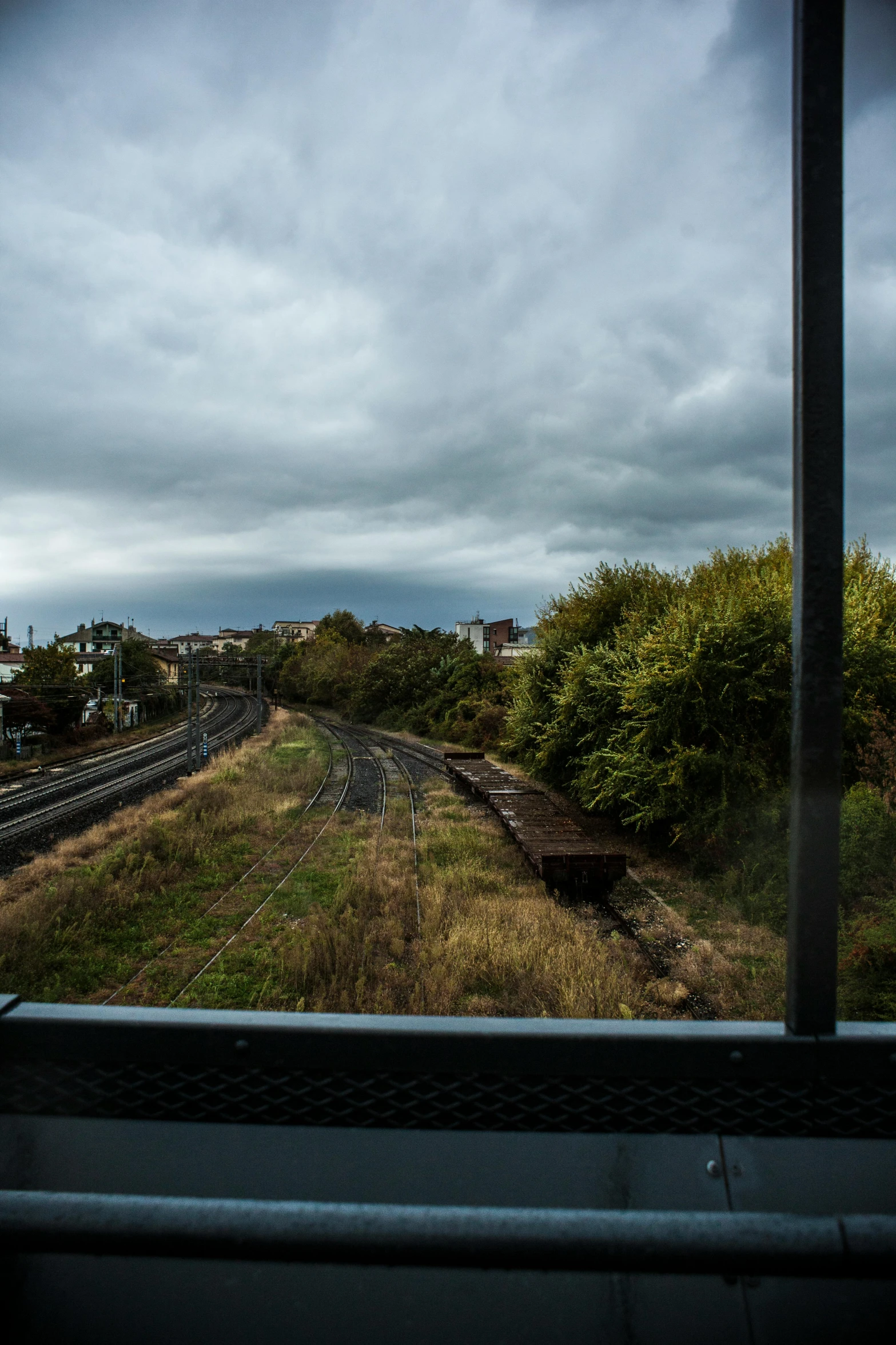 a view of a train track through a window, grey cloudy skies, opposite of urban sprawl, autumn rain turkel, trams