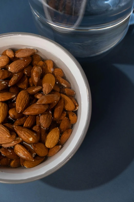 a bowl of almonds next to a glass of water, renaissance, detailed product image, alternate angle, mid - shot, maple syrup sea