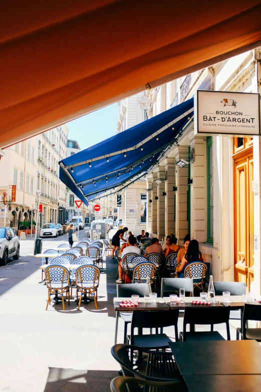 a city street filled with lots of tables and chairs, blue shutters on windows, wearing a french beret, canopies, exterior