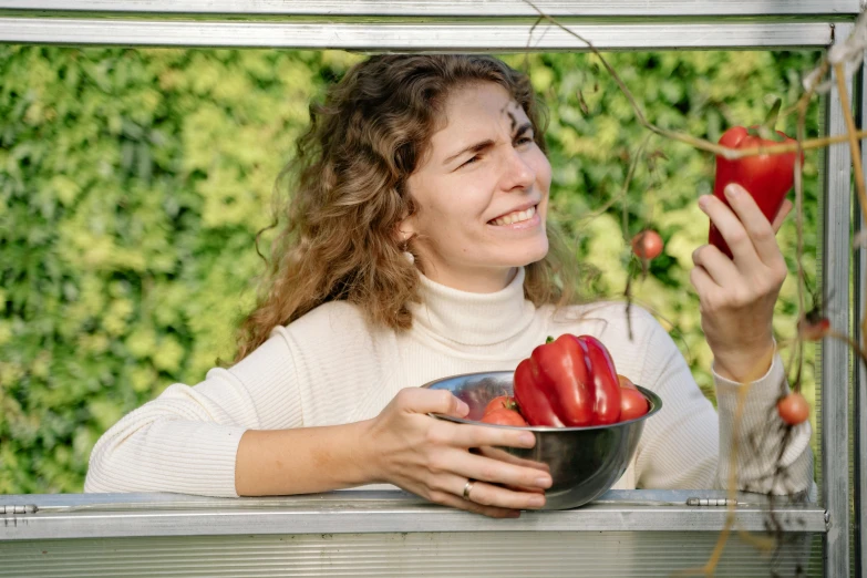 a woman holding a bowl of strawberries and an apple, by Julia Pishtar, pexels contest winner, looking outside, hydroponic farms, paprika, amused