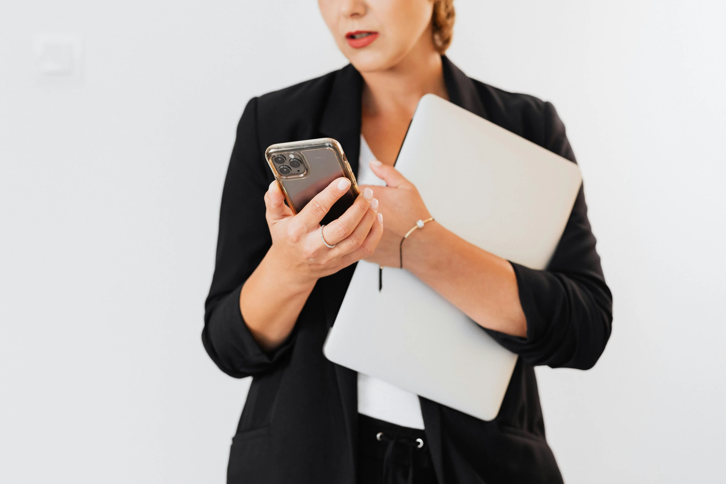 a woman holding a laptop and a cell phone, by Carey Morris, trending on pexels, wearing black suit, white backround, taken on iphone 14 pro, 1450