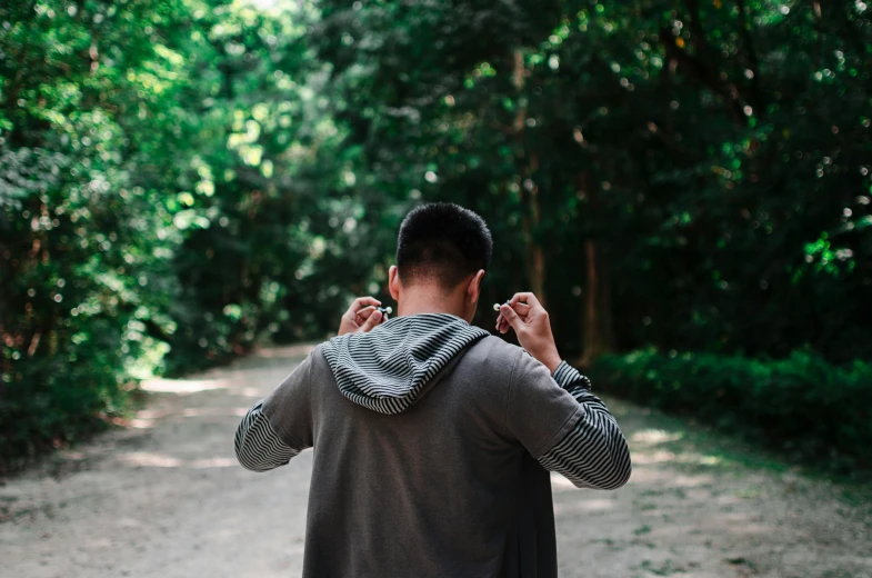 a man walking down a dirt road talking on a cell phone, pexels contest winner, grey hoodie opened, placed in a lush forest, showing her shoulder from back, getting ready to fight