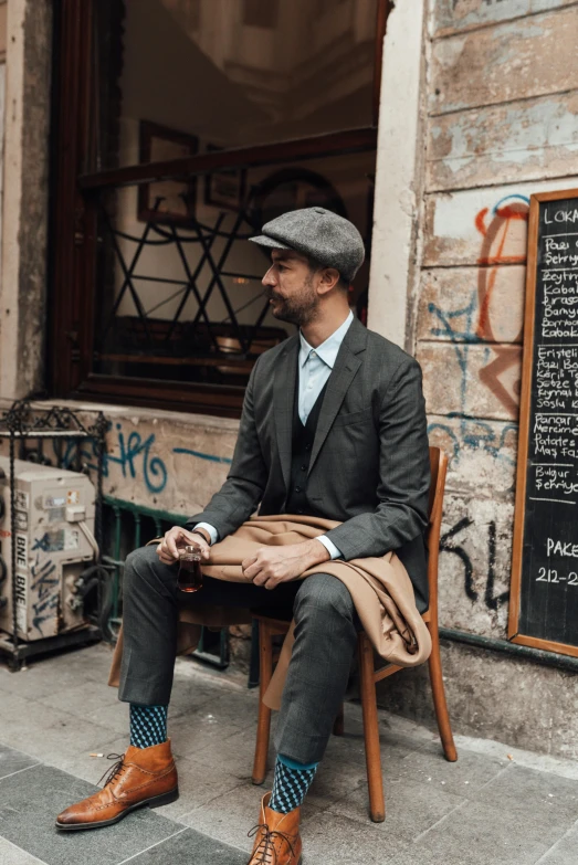 a man sitting on a chair in front of a building, dapper, milan jozing, curated collections, at a city street