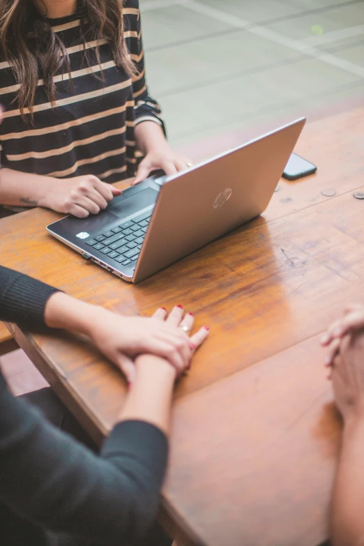 two women sitting at a table with a laptop, by Carey Morris, pexels, bottom angle, four hands, teaching, on wooden table