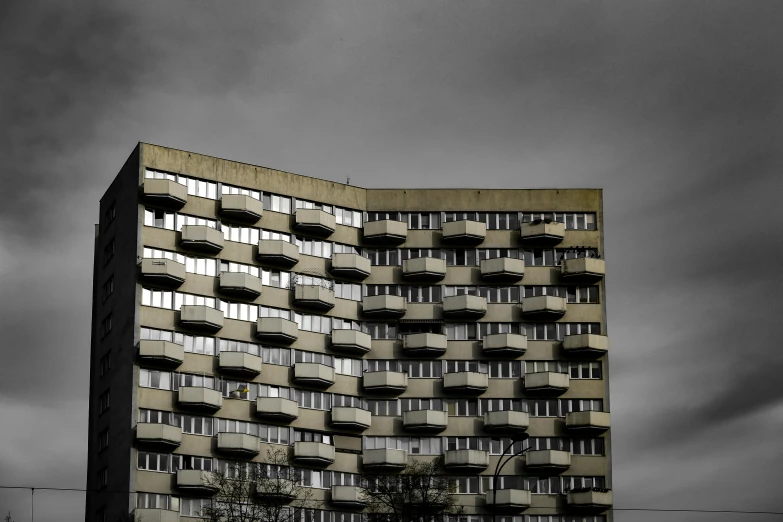 a black and white photo of a tall building, unsplash, brutalism, abandoned prague, ten flats, balconies, dark sky