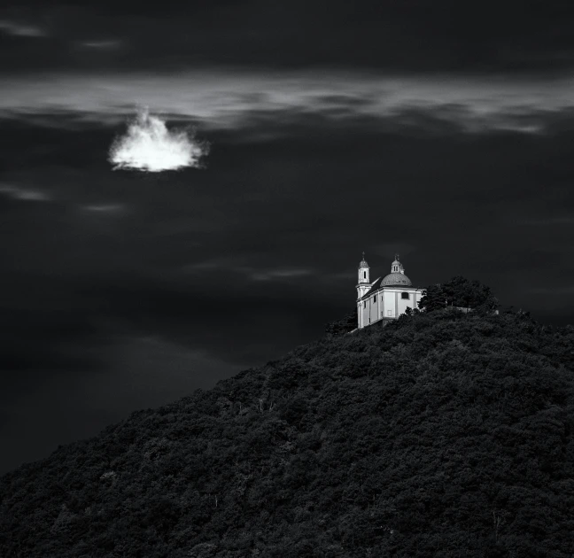 black and white pograph of a small building on a hill with clouds above