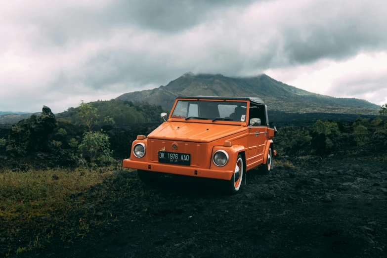 an orange convertible parked in the middle of some dirt