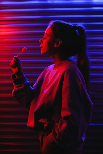 a woman standing in front of a red and blue light, pexels contest winner, lollipop, eating, woman in streetwear, holding wands