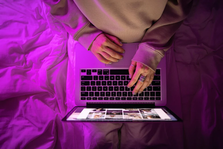 a person using a laptop computer on a bed, an album cover, trending on pexels, computer art, soft neon purple lighting, high angle shot, purple outfit, non-binary