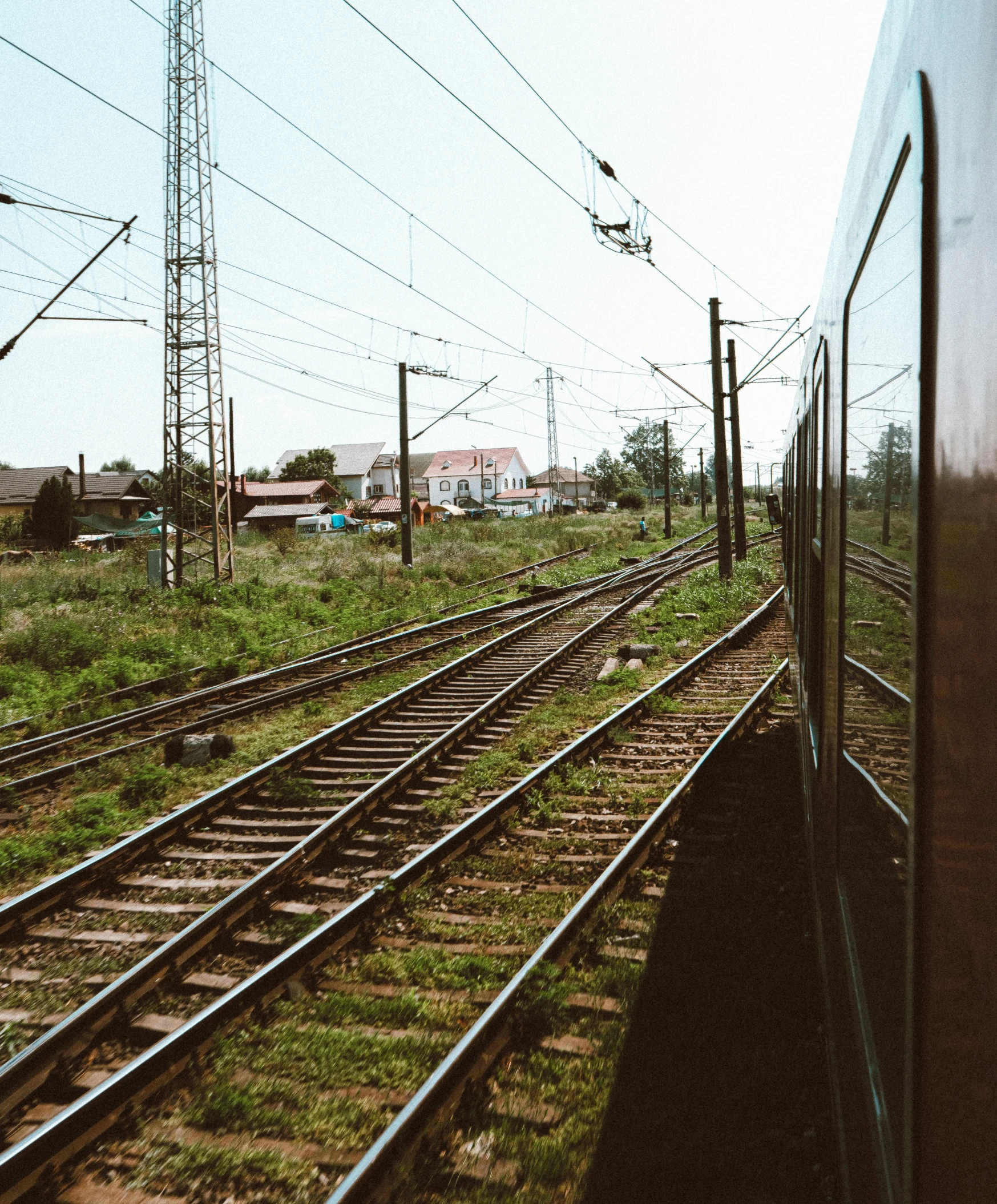 a train traveling down train tracks next to a lush green field, unsplash, regionalism, low quality photo, ground level view of soviet town, black wired cables, 🚿🗝📝
