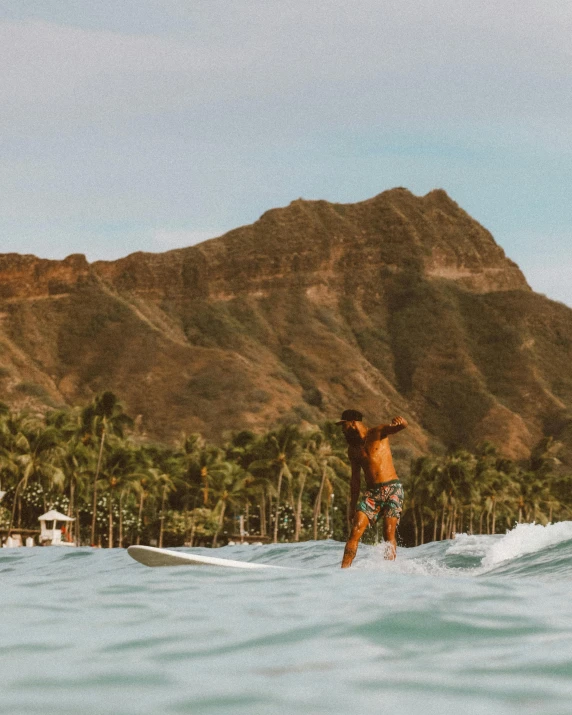 a man riding a surfboard on top of a wave, by Robbie Trevino, pexels contest winner, posing in waikiki, mountains in the background, gif, beach trees in the background